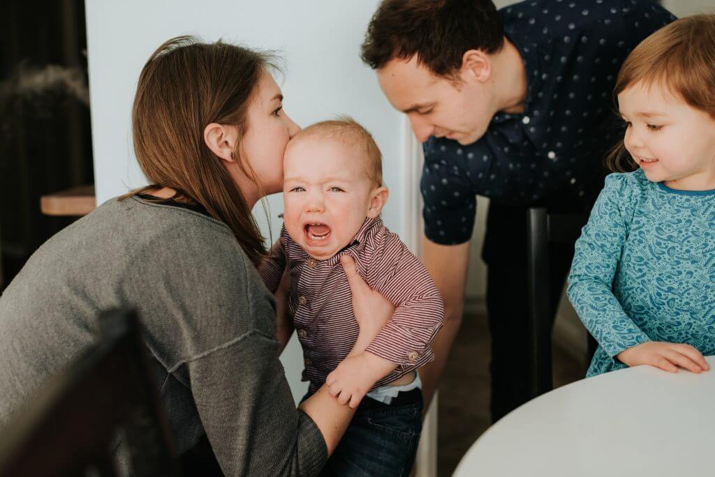 Mid adult couple with toddler daughter and crying baby son in living room