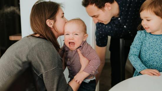 Mid adult couple with toddler daughter and crying baby son in living room